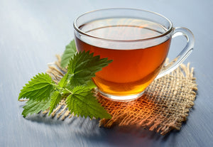 Tea in a cup beside fresh tea leaves